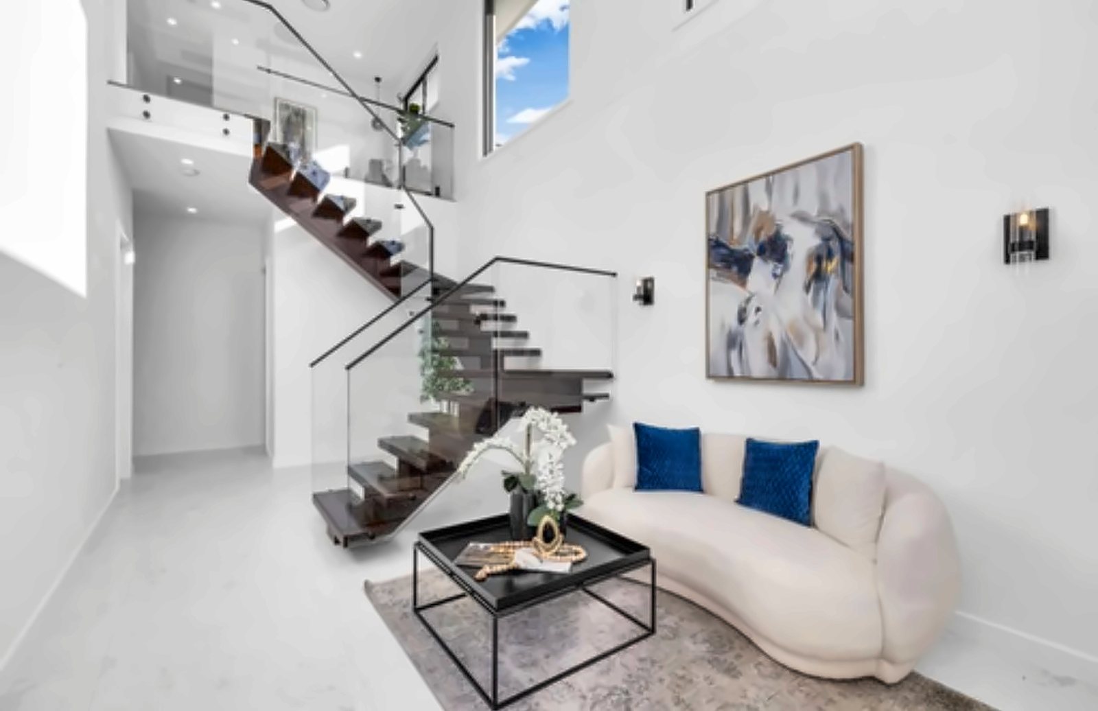 A floating timber staircase with a glass balustrade rising through a bright double-height void
